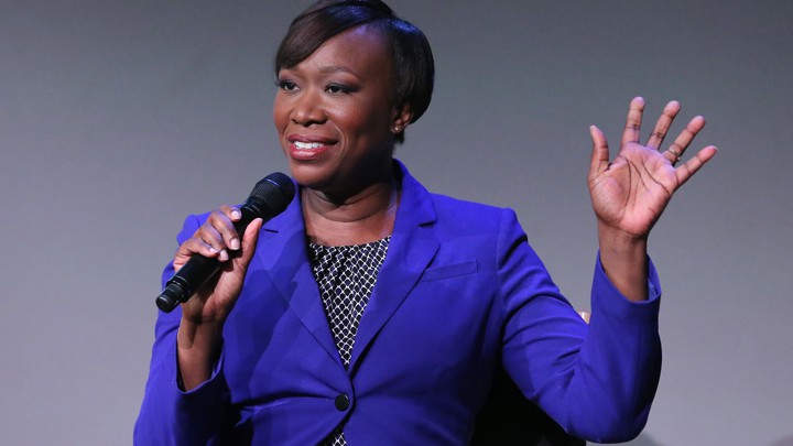 Joy Reid wearing a purple blazer and holding a microphone