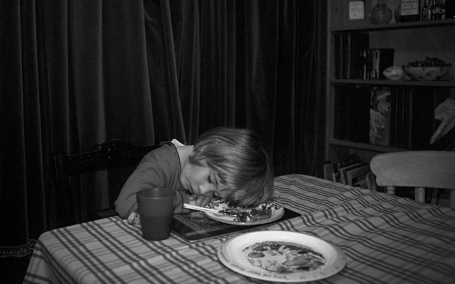 A black-and-white photo of a young girl asleep at the dinner table