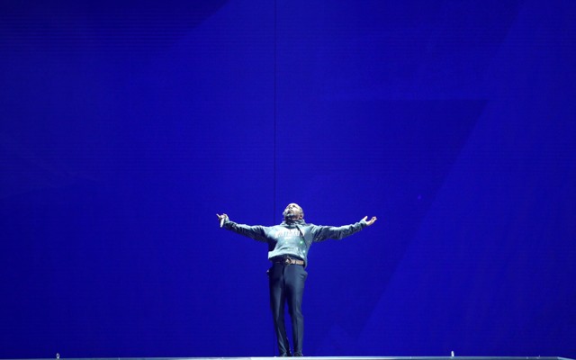Kendrick Lamar performing onstage against a blue backdrop