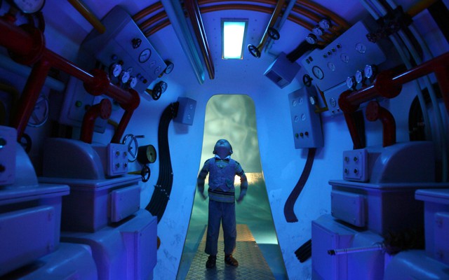 A boy stands in a submarine, looking up. 