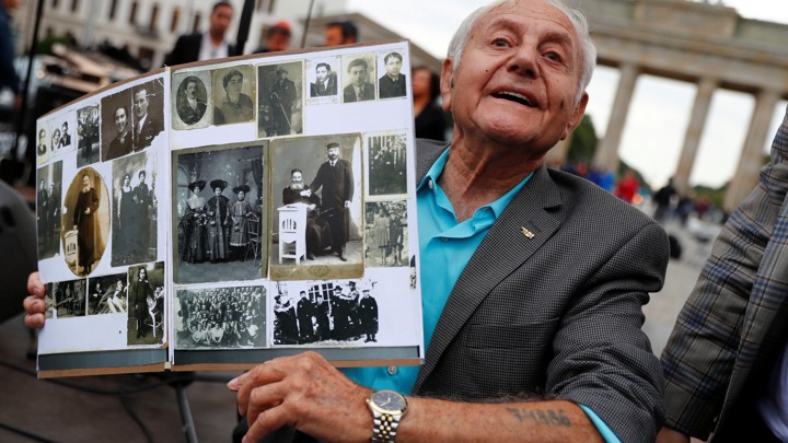 Holocaust survivor Morris Dan shows family photographs as he poses in front of the Brandenburg Gate in Berlin in 2017.