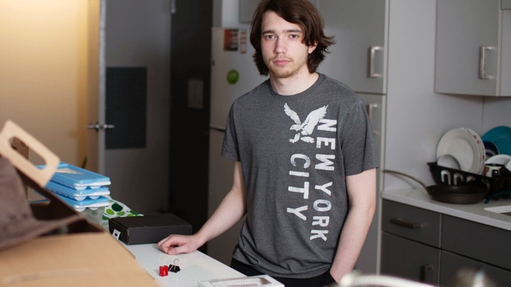 A boy wearing a gray shirt stands near a counter.