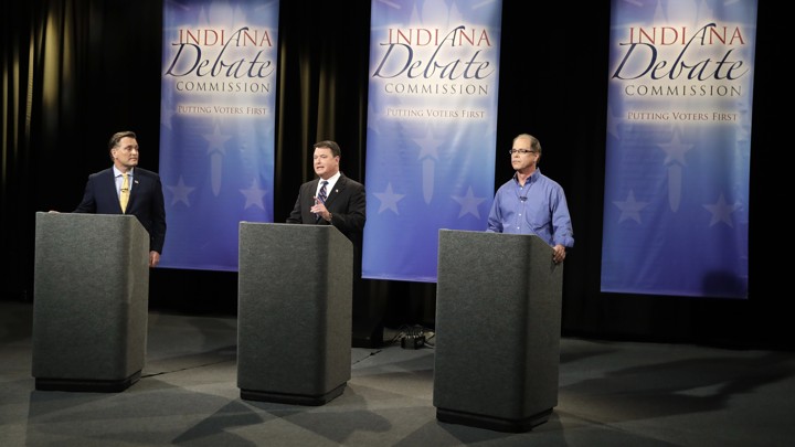 Three senatorial candidates stand at lecterns on a debate stage.
