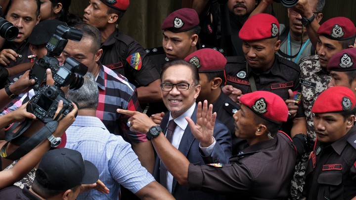 Anwar smiles and waves in between police officers and press photographers