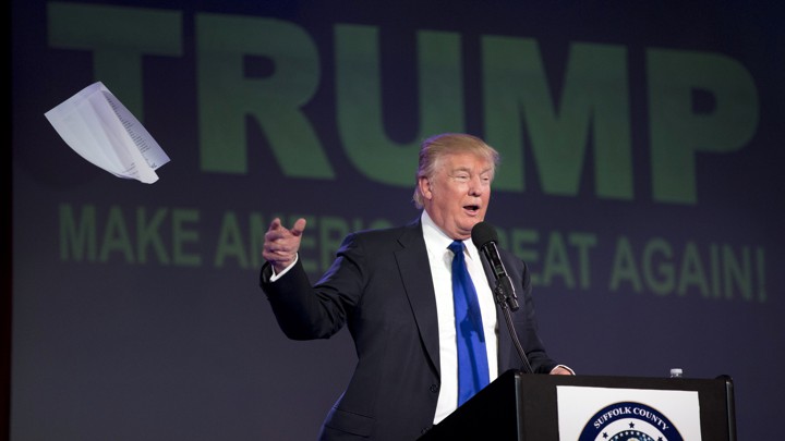 Donald Trump speaks at a podium while tossing away a pile of notes.