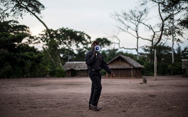A health worker holds a megaphone to his mouth while standing on a patch of dirt.