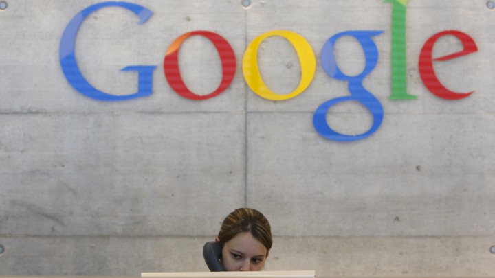 A receptionist speaks on a phone under a Google logo.