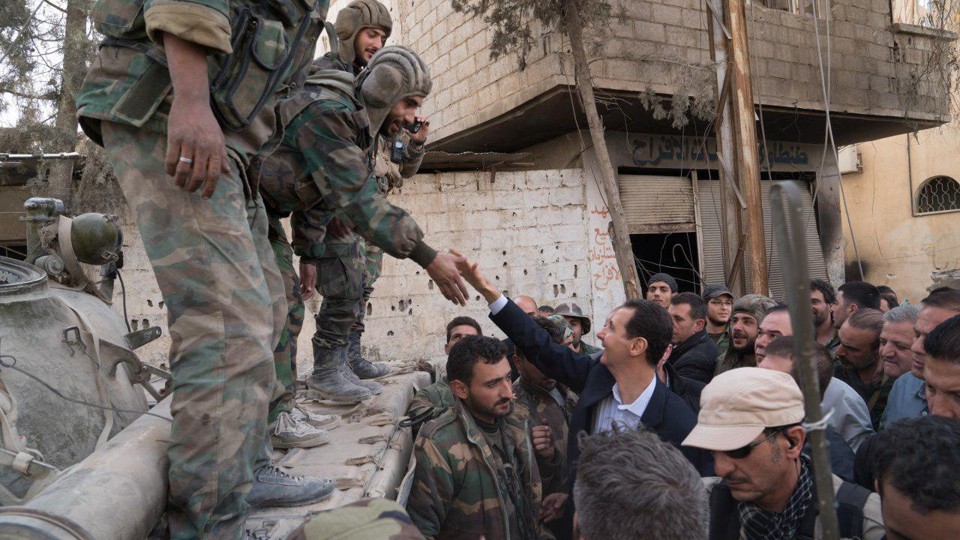 A soldier reaching down to shake President Assad's hand