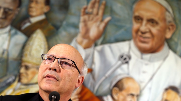 Pérez speaking in front of a mural of Pope Francis