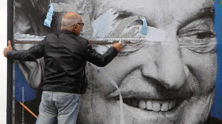 A man tearing a poster of George Soros's face