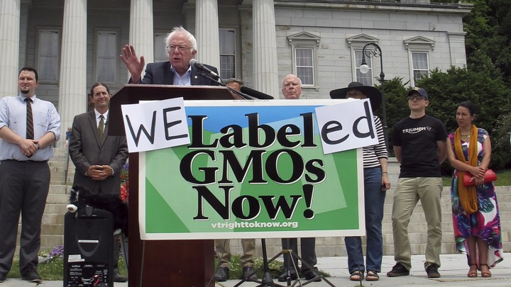 Bernie Sanders behind sign that says "We Labeled GMOs Now!"