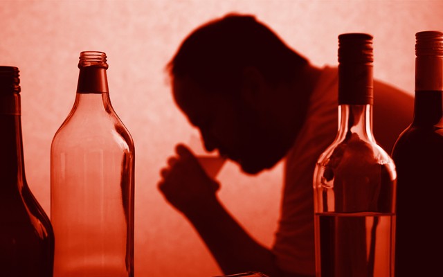 A silhouette of a man drinking from a cup next to bottles of wine and liquor