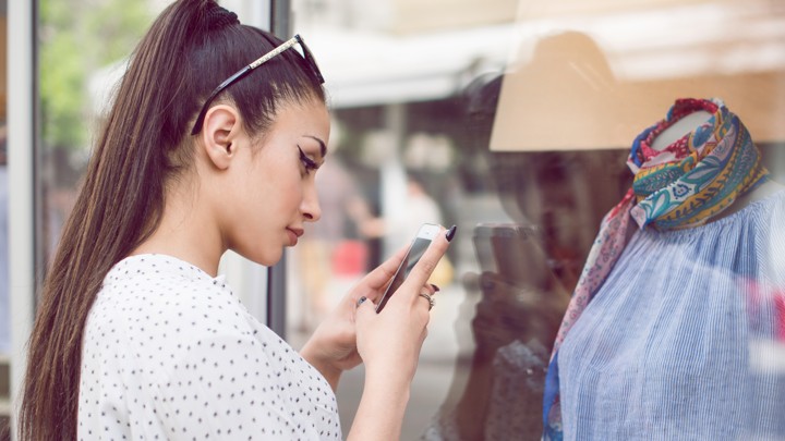A woman uses a smartphone to take a picture of clothing on a mannequin.