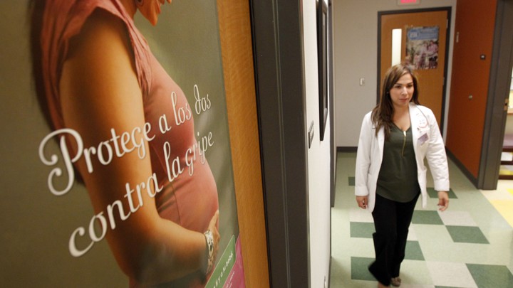 A woman walks through a clinic with a poster of a pregnant woman on the wall.