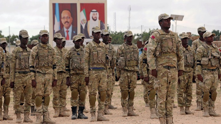 Soldiers standing at attention in front of pictures of state leaders