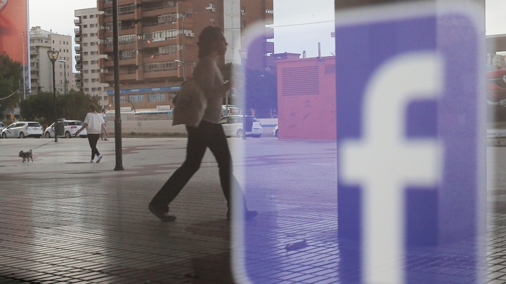 People walk past a Facebook logo on a shop window