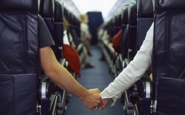 Two people hold hands across an airplane aisle
