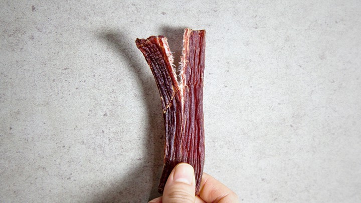 A hand holding a torn piece of beef jerky