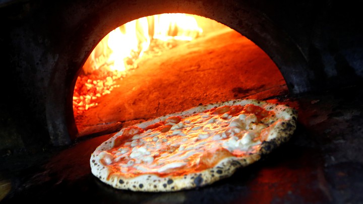 A pizza in front of an open brick oven