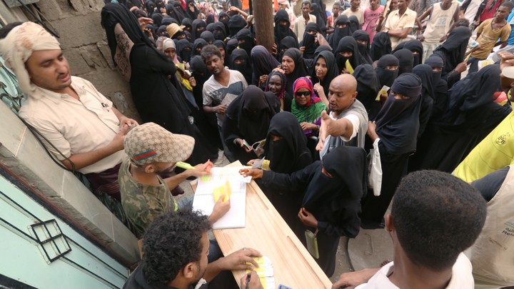 Several Hodeidah residents wait in front of a table, where workers distribute aid materials.