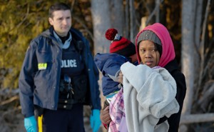 RCMP officer looks on as a woman carrying a child waits to cross the U.S.-Canada border.