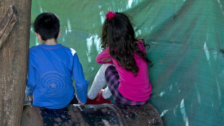 A boy and a girl sit on a barrel with their backs to the camera