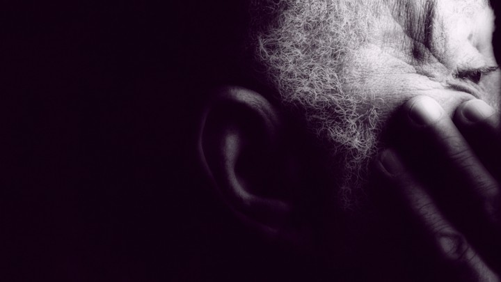 An older man rests his hand on his face.