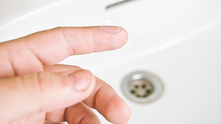 A finger holds a contact lense over a sink
