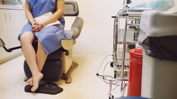 A woman sits in an examination room while wearing a hospital gown