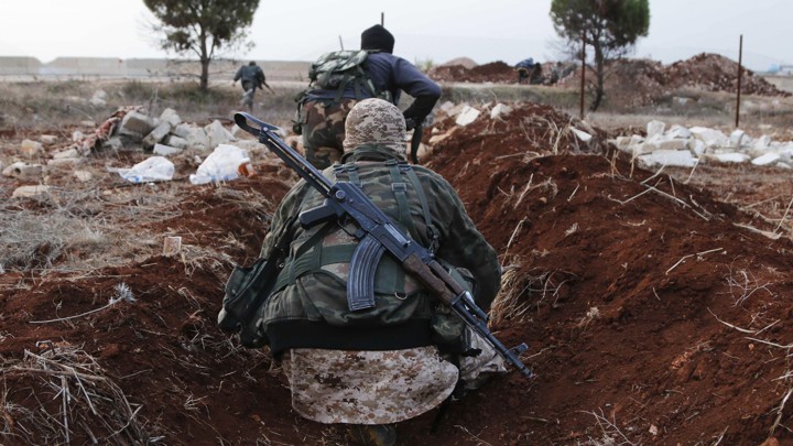 Two members of al-Qaeda's Nusra Front in Syria hold weapons while standing in a ditch.