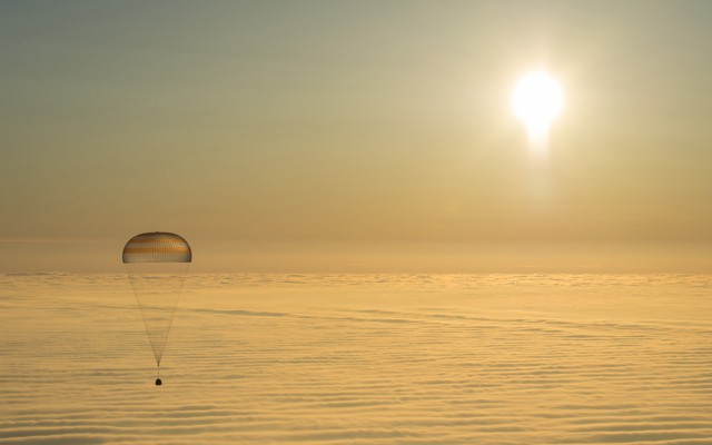 An astronaut capsule with a parachute floats down to Earth.