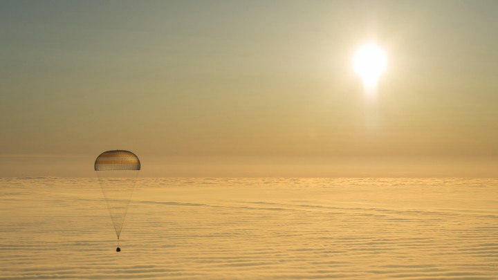 An astronaut capsule with a parachute floats down to Earth.
