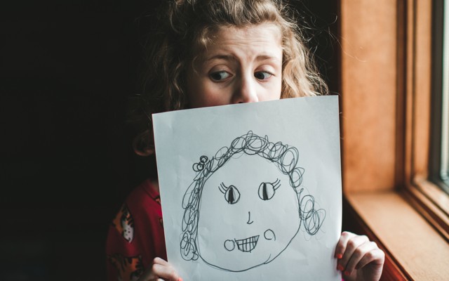 A little girl holds up a picture of herself that she has drawn.