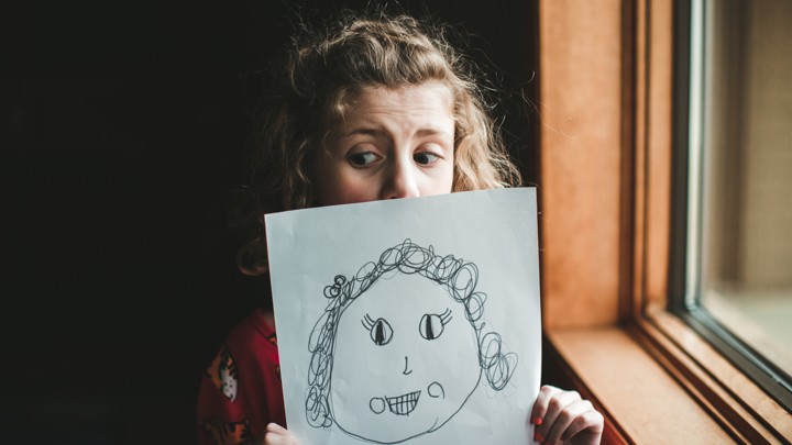 A little girl holds up a picture of herself that she has drawn.