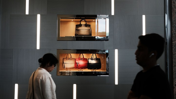 People walk in front of a display of handbags