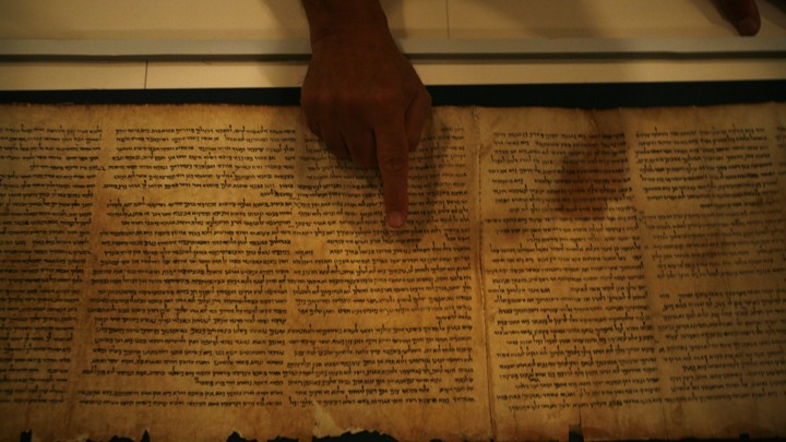 A person points with their index finger at the Isaiah Scroll.