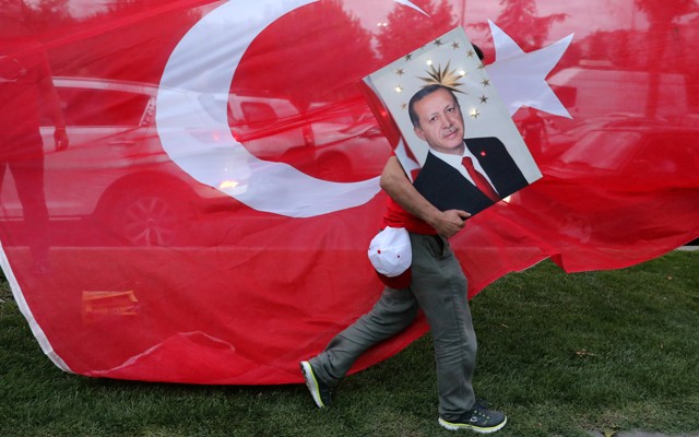 An Erdoğan supporter carries a poster with his face in front of a Turkish flag.