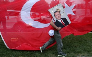 An Erdoğan supporter carries a poster with his face in front of a Turkish flag.