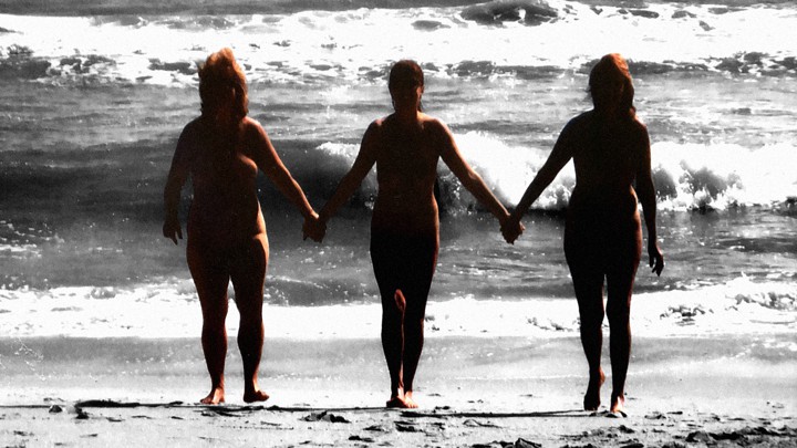 Three nude sisters hold hands on the beach