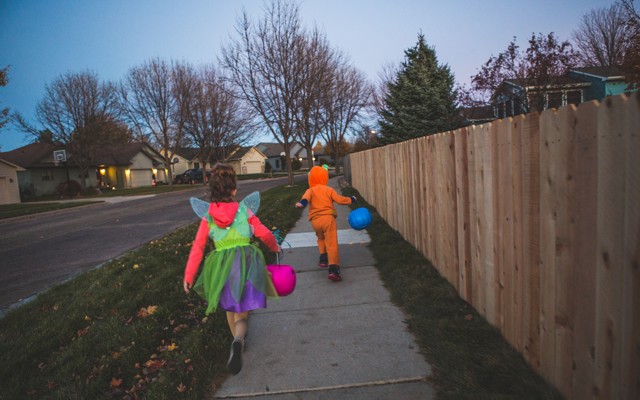 A girl and a boy in Halloween costumes run down an empty sidewalk