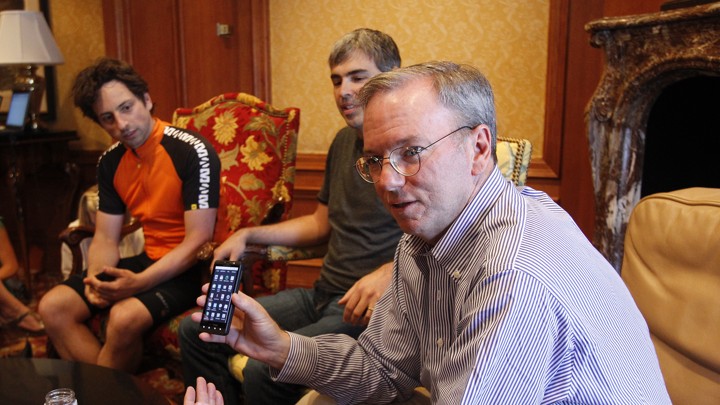 One man holds up an Android phone while two others look on.