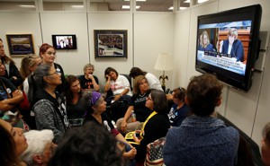 People crowd into a room to watch Christine Blasey Ford testify on TV.