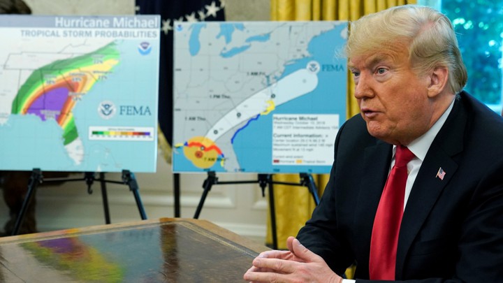 President Trump sits at a desk in front of diagrams of Hurricane Michael's path.