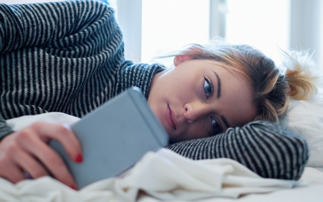 A woman stares at her phone in bed