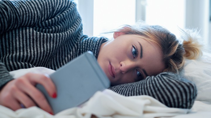 A woman stares at her phone in bed.