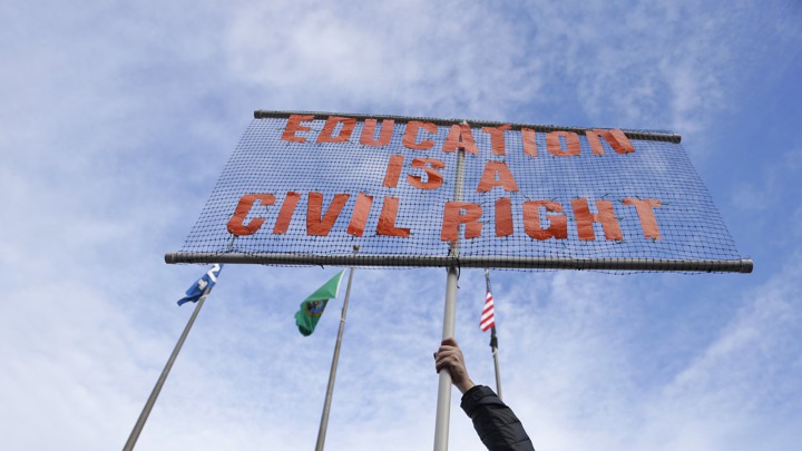 A public-school teacher in Washington State holds a sign at a 2017 rally calling for more equitable school funding.