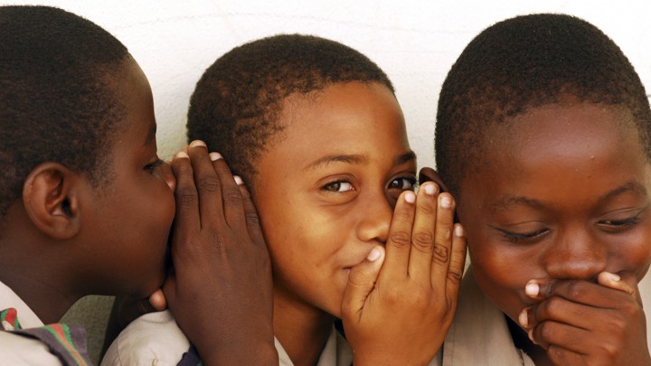 Three children whisper into one another's ears.