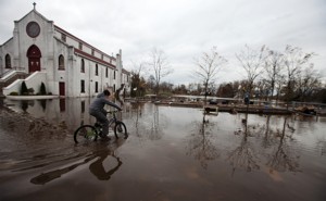A person rides a bicycle past a church on a flooded street.