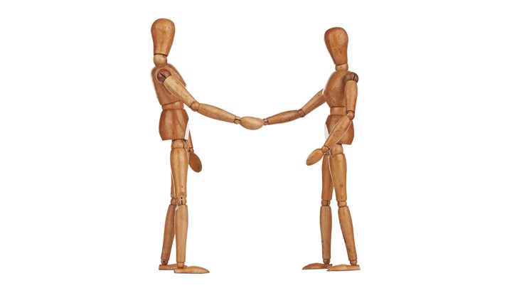 Two stick-figure wooden models shake hands.