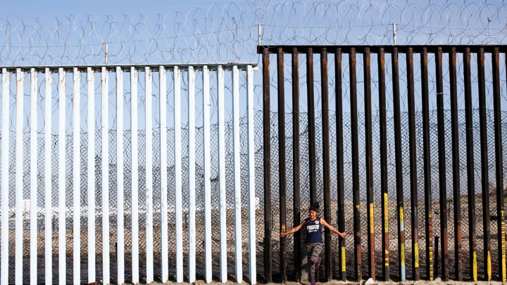 A woman leans against the U.S.-Mexico border wall